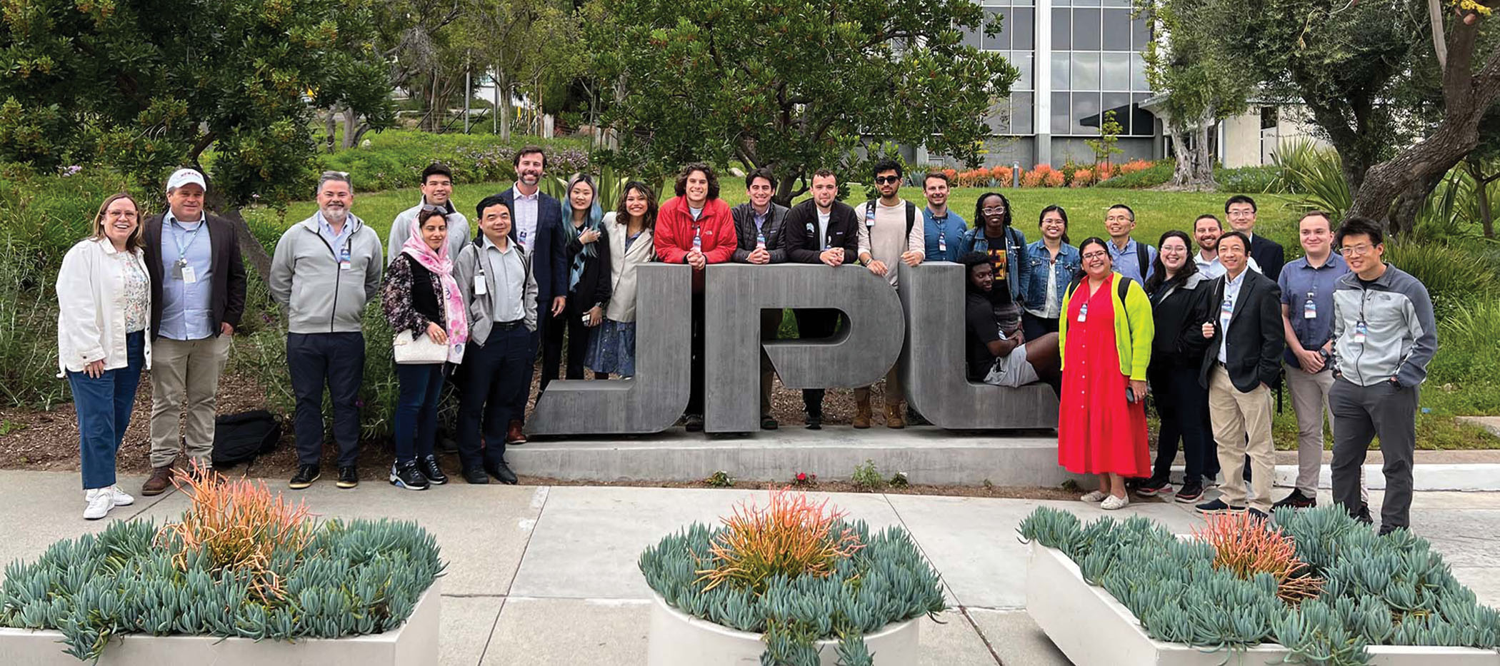 A large group of I-Corps participants stand outside near a stone structure that says "JPL."